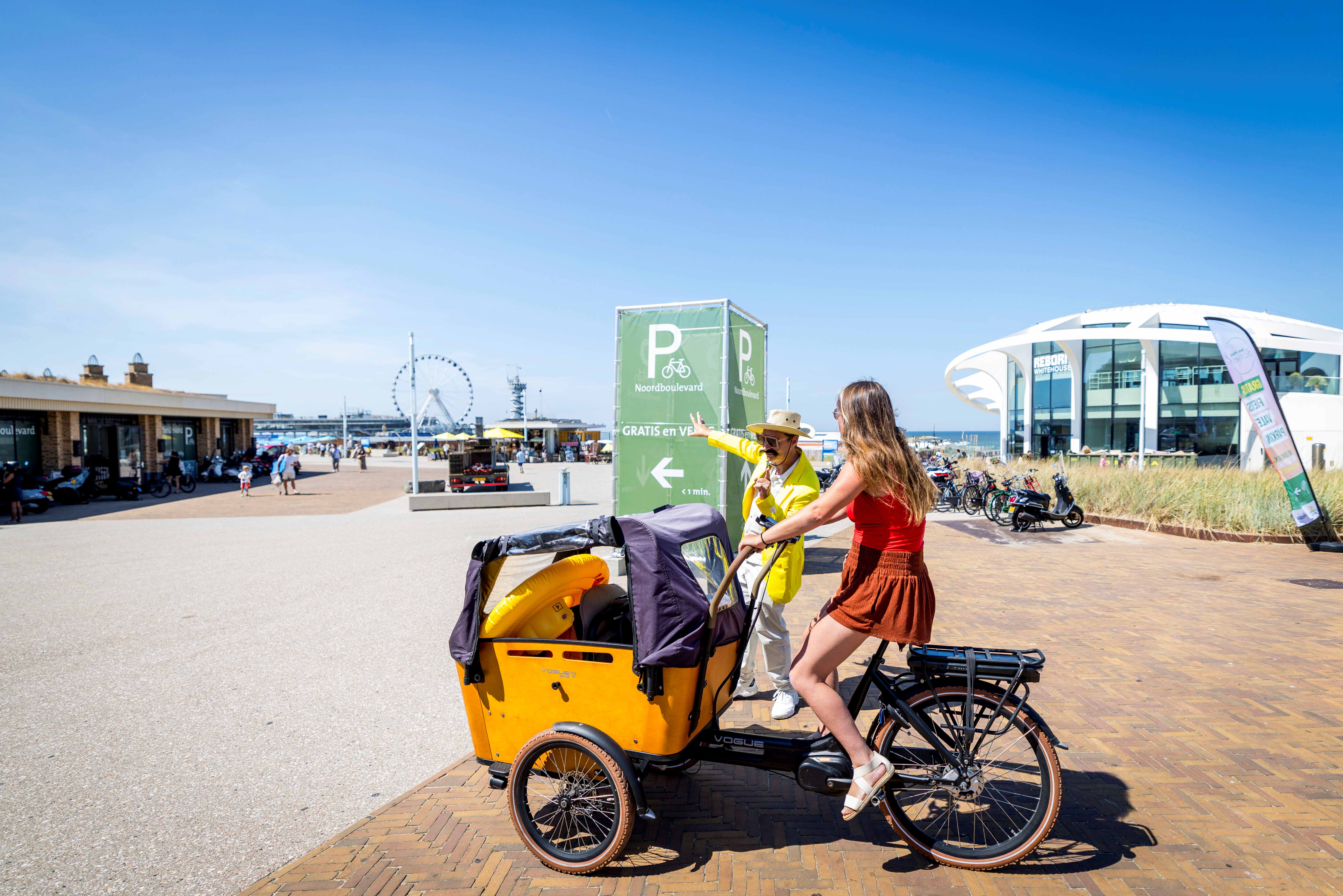 Actie fietsenstalling Noordboulevard Scheveningen waar acteur verwijst naar stalling voor bezoeker vrouw met bakfiets.